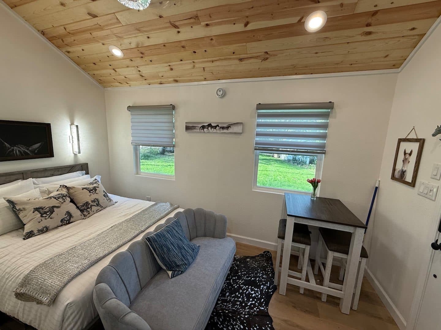 Cabin interior with a bed, loveseat and small dining table under a wood ceiling