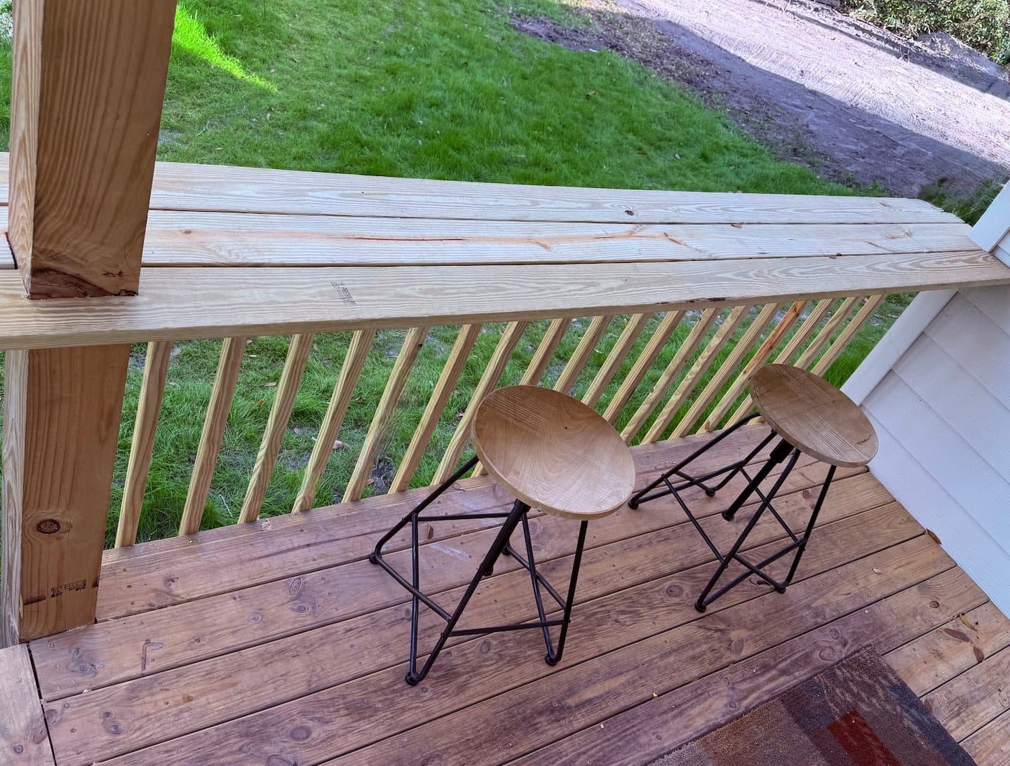 Porch with two stools at a wooden railing overlooking the lawn