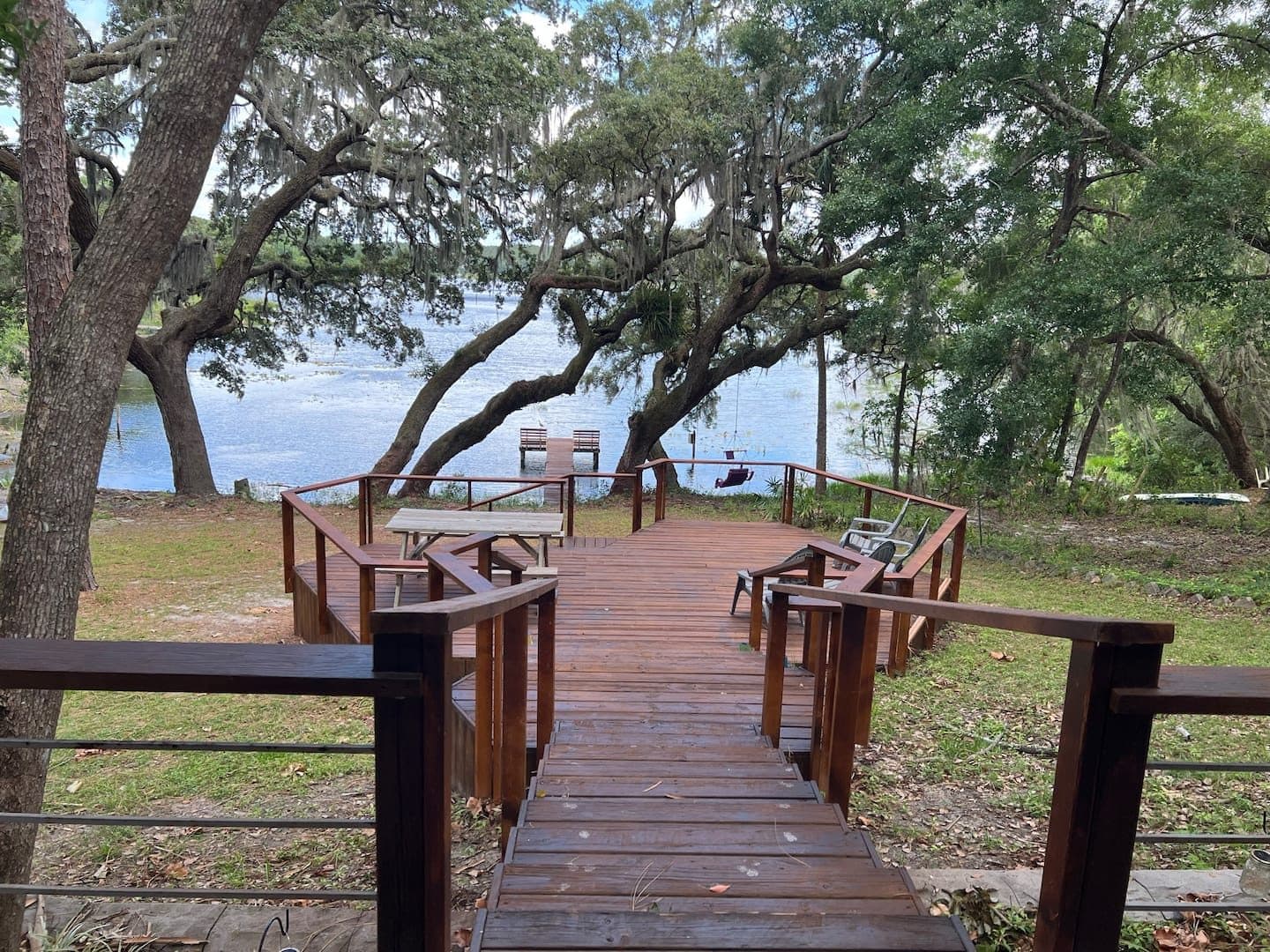 Wooden boardwalk with railings leading through oak trees toward the lake